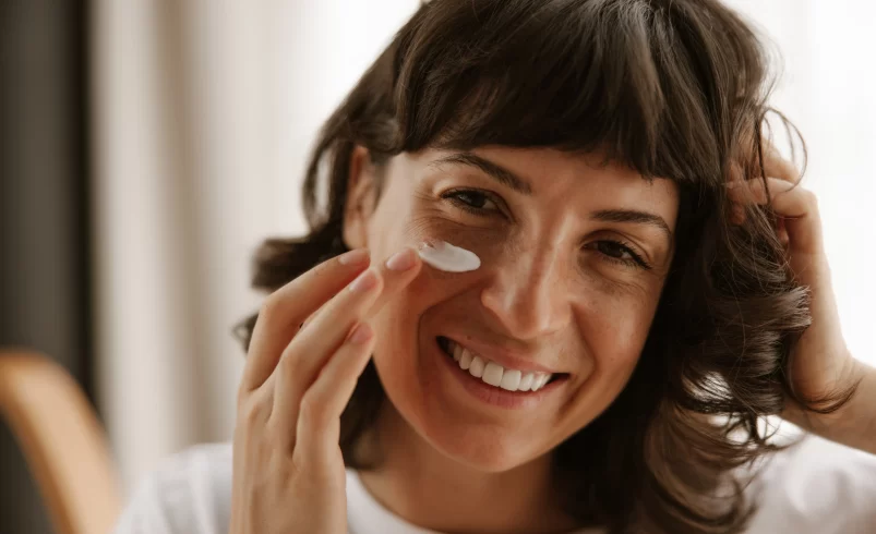 Usměvavá žena si aplikuje hydratační krém
