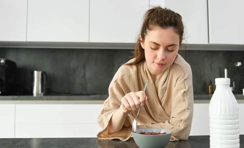 Žena snídá jogurt a cereálie